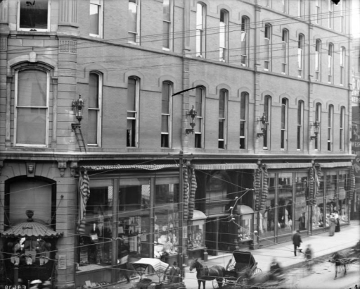 View of the Daniels and Fisher store in Denver, Colorado; shows glass storefront windows, exterior sconce lamps, and a horse and buggy.