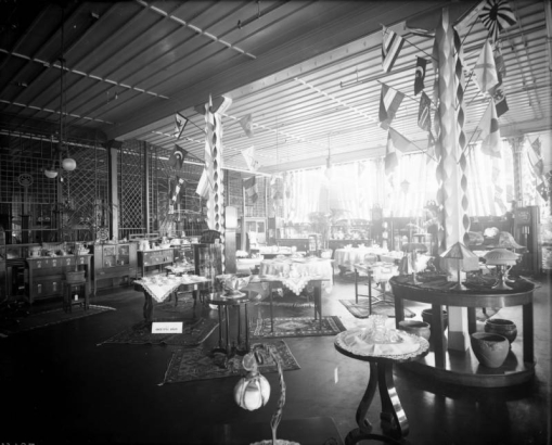 Interior view of the Daniels and Fisher store in Denver, Colorado; shows crystal, china, lamps, pottery, buffets, palms, a wooden screen, and International flags. Sign reads: "Oriental Rugs."