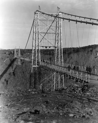Tourists walk across the Royal Gorge Suspension Bridge, Fremont County, Colorado, over 1000 feet above the Arkansas River. American flags decorate the tall towers for the dedication of the 1260 foot long and 18 feet wide bridge. Built by the Royal Gorge Bridge and Amusement Company in six months, dedicated on December 6, 1929.