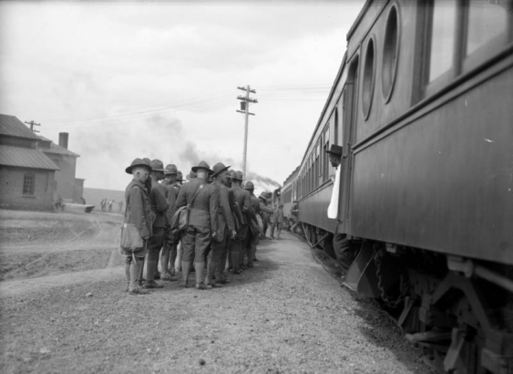 Uniformed troops of infantry men board a Denver and Rio Grande train of Pullman sleeping cars, about to depart Fort Logan, a World War I assembly point for young soldiers, Colorado. Many wear uniforms consisting of jackets, jodhpurs, gaiters, boots and wide brim hats with Montana creases. A Black man, possibly a porter, stand in doorway of one of the cars. He wears a white coat and dark hat.