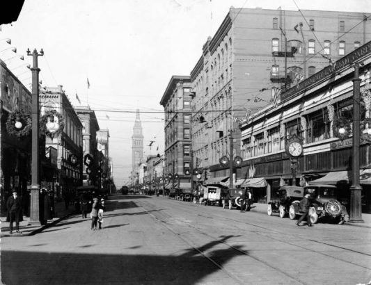 View of 16th (Sixteenth) at Welton Street in Denver, Colorado; shows automobiles, pedestrians, the Mack Block, the Daniels and Fisher tower, a clock with letters: "Sam Mayer," and Christmas wreaths.