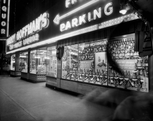 Night view of Harry Hoffman's Cut Price Liquor store at Curtis and 18th (Eighteenth) Streets in Denver, Colorado. Windows display bottles of Calvert whiskey; neon signs read "Harry Hoffman's," "Liquor," and "Free Parking."