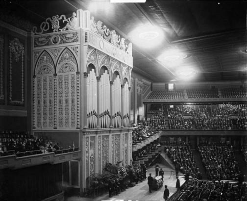Interior view at the Denver Municipal Auditorium in Denver, Colorado; shows an audience, a pipe organ, and a coffin at the funeral of Mayor Robert Speer.