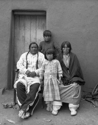 Portrait of a Native American (Taos Pueblo) family: a man identified as Antonio Romero (wearing beaded moccasins), his wife and children, a boy and a girl.