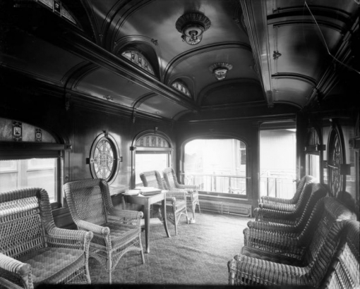 Shows the interior of the San Benito Car, possibly from the Midland Railroad company, Colorado. The railway car has two wheel windows, possibly electric lights and wicker chairs.