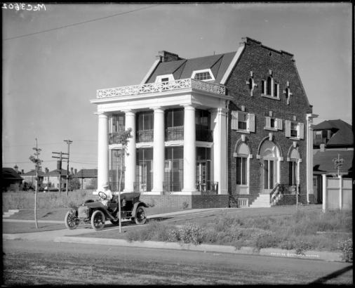 View of the residence of Margaret Long, a Denver physician, at 2070 North Colorado Boulevard in Denver, Colorado; a woman (possibly Margaret Long) sits in an automobile parked in the driveway.
