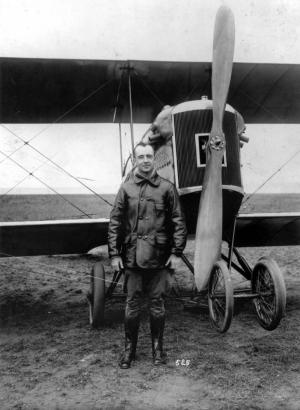 First Lieutenant John F. Curry poses by the propeller of an airplane; This first national commander of the CAP (Colorado Air Patrol) wears an outfit including a flight jacket and boots.