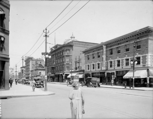 View of the Empire and Adams Hotels on 18th (Eighteenth) Street at Glenarm Place in downtown Denver, Colorado. Automobiles and pedestrians are on the street. Signs read: "W. B. Magby," "Empire Hotel," "Bail Bros.," and "The Adams."