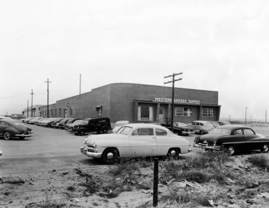 View of Western Bakers Supply, at 4969 Colorado Boulevard, in Denver, Colorado; shows a brick building, and parked cars. A van reads: "Cunningham's Restaurant."