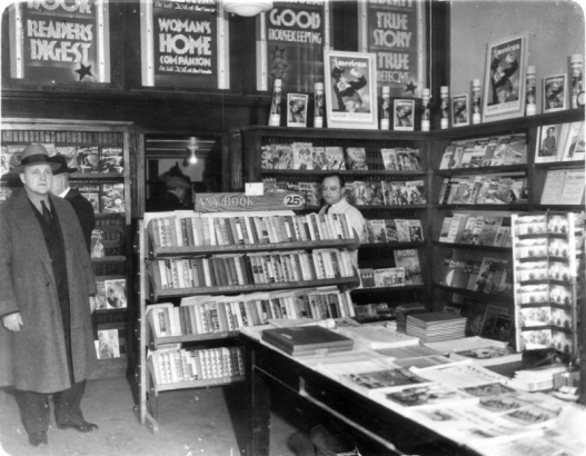 Interior view of a book store in Denver, Colorado; shows books, magazines, and men identified as Detective John Wells (topcoat and fedora hat) and Sam Handler.