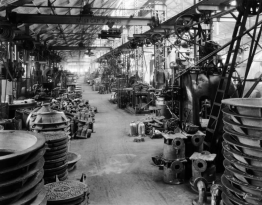 Interior view of the machine shop of General Iron Works at 1245 Osage Street in the Lincoln Park neighborhood of Denver, Colorado. Manhole covers, molds, machinery, and mobile overhead cranes are in the warehouse building.