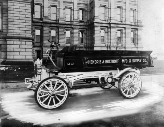 View of a Hendrie and Bolthoff Manufacturing Supply delivery truck parked near the Colorado State Capitol building in Denver, Colorado. Lettering on the open-cab truck reads: "22 The Hendrie & Bolthoff Mfg. & Supply Co."