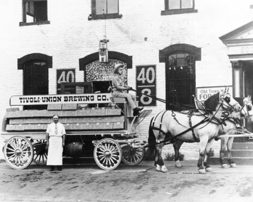 View of a horse drawn wagon in Denver, Colorado; men pose; sign reads: "Tivoli-Union Brewery."