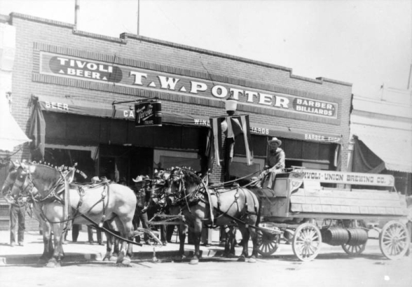 View of the Tivoli Union Brewery beer wagon and team of horses, in Denver, Colorado; storefront sign reads: "Tivoli Beer T.W. Potter Barber Billiards."