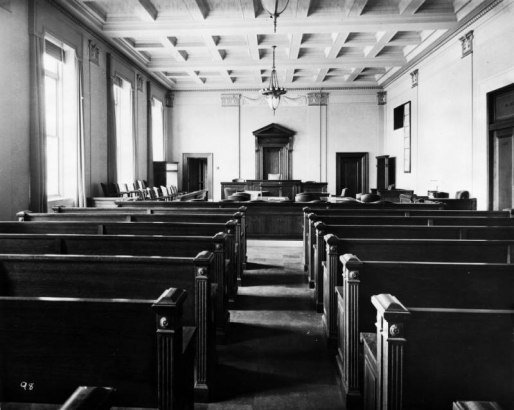 Interior view of a courtroom at the City and County Building in Denver, Colorado. The room has ornate trim and a chandelier.