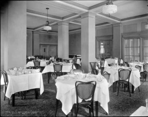 Interior view of dining room, Colburn Hotel, Denver, Colorado; shows cane-backed chairs and tables set with tablecloths and dinnerware.
