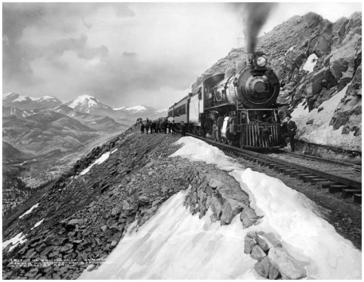View of Denver, Northwestern & Pacific Railway (later called Denver & Salt Lake) engine number 100 & passenger train approaching Rollins Pass, Colorado; group of people standing beside standard gauge track & train, snowfields; Moffat Road, Continental Divide; Rocky Mountains, background left .