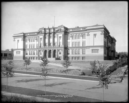 Exterior view of North Denver High School, 2960 North Speer Boulevard, Denver, Colorado; built in 1911 and ready for students in September, landscaping and sidewalk construction still in progress; best example of Beaux-Arts style of architecture with recessed arched portals, Ionic columns, broken pediments & finials, ornate facade with rooftop balustrade, cost $335,000 with 102 rooms designed by architect David W. Dryden.