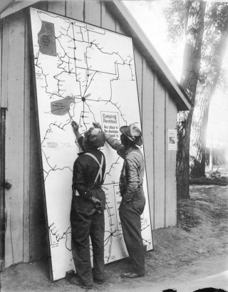 Men look at a map of Colorado at City Park in Denver, Colorado; lettering reads: "Camping Permitted Any Place in the Mountains Not Fenced In."