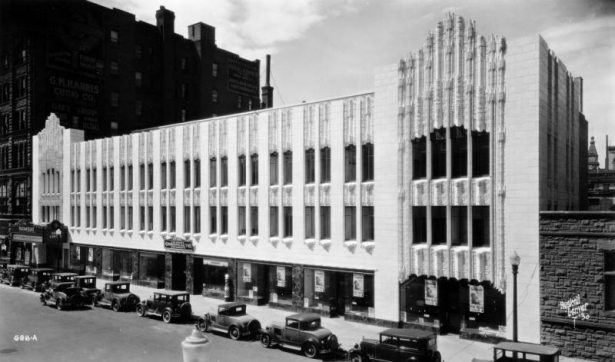 View of the art-deco style Paramount Theater building, designed by Temple Hoyne Buell, at 16th (Sixteenth) and Glenarm Streets in downtown Denver, Colorado. Automobiles are parked nearby. Signs in the window read: "Richard Barthelmess Dawn Patrol Tabor Theater [...]" and "New Home Colorado Chiropractic University."