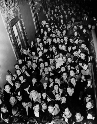 Boys and girls crowd into a hallway of the Paramount Theater designed by Temple Hoyne Buell at 16th (Sixteenth) and Glenarm Streets in Denver, Colorado. The children wait to be seated for a free movie.