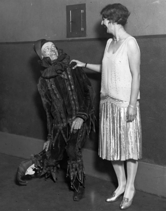 Portrait of Denver Community Players in Denver, Colorado; William Myatt is in a jester costume, a woman in a satin flapper outfit looks on.