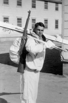 John D. Magrath, a member of the 10th Mountain Division 85th Regiment, Company G and a recipient of the Congressional Medal of Honor, poses outdoors with skis and poles at Camp Hale (Eagle County), Colorado. He wears a backpack with rifle, jacket, and mittens.