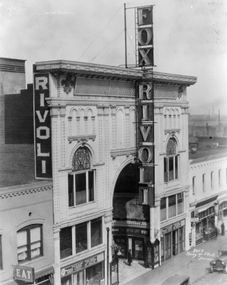 Rooftop view of the Rivoli Theater at 1741 Curtis Street in downtown Denver, Colorado. The four-story building has an ornate entryway decorated with electric lights. Signs read: "Fox Rivoli," "Thos. H Ince's Great Drama 'The Cup of Life,'" and "Hotel Elwood."
