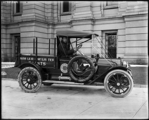 View of a delivery truck in Denver, Colorado; shows a man driving, tire chains, and lettering: "Kohler-McLister Paints - the Mark of Quality" and "1621 Arapahoe St."