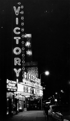Night view of the Victory Theater in Denver, Colorado; neon signs and marquee read: "Victory, Girls, Fun For Adults Only, Girlesque, Acapulco Uncensored, Big Sin City, Spicy Films," and "Discount Credit Jewelers."