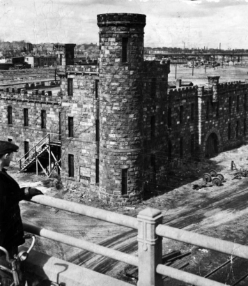A boy with a bicycle stands on the 16th (Sixteenth) Street Viaduct near Walker Castle (Castle of Culture and Commerce) in Riverfront Park, Denver, Colorado. The stone castle has a round turret and battlements.