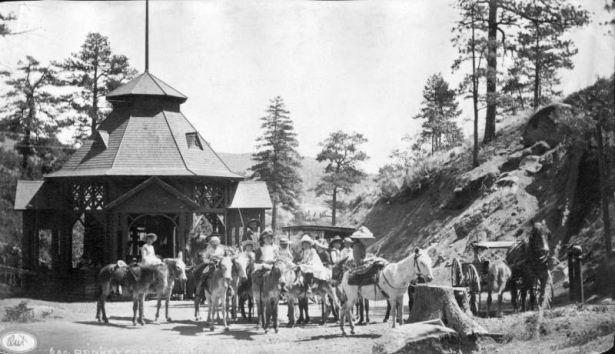 View of group of girls on donkeys with man, carriage and ornate gazebo at Ute Iron Spring Chateau, Manitou Springs, El Paso County, Colorado.