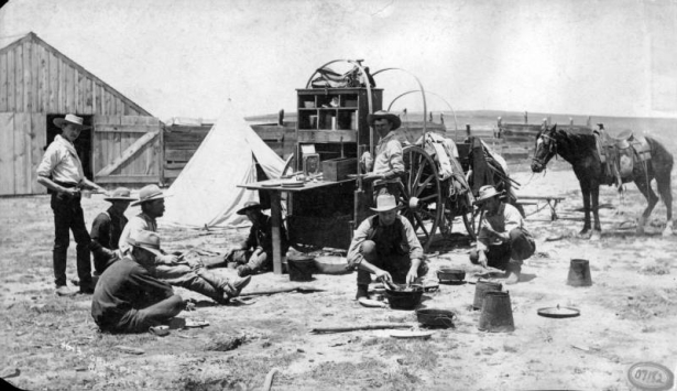 View of group of men with meal at chuckwagon, shows barn, tent and horse, Colorado.