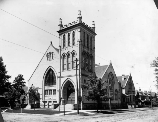 View of the First Avenue Presbyterian Church at 120 West First Avenue in the Baker neighborhood of Denver, Colorado. The brick church has a bell tower with arched windows and battlements, stained glass windows, and an arched entryway.