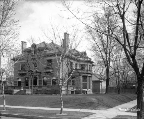 View of the Temple Buell house at 906 Grant Street in the Capitol Hill neighborhood of Denver, Colorado. The two-story brick house has a tile roof, chimneys, circular and arched windows, stone balconies, and a large patio.