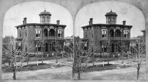 View of the William Bradley Daniels house at 14th (Fourteenth) and Curtis Streets in downtown Denver, Colorado. The Italianate-style house has a low pitch roof, cupola, contrasting hood molds, and covered balconies and porches.