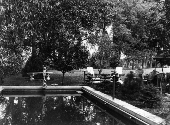 View of a pool and lawn furniture at the George W. Gano house in Englewood (Arapahoe County), Colorado. A terra-cotta statue of a boy is at one end of the pool. Trees are nearby.