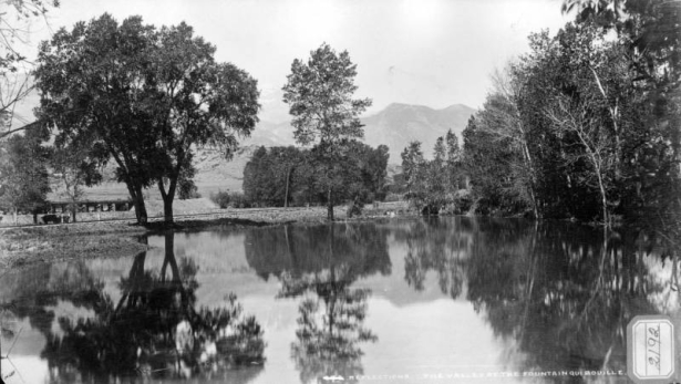 View of mountain and tree reflections in pool on Fountain Creek with railroad tracks, trestle, and cattle, El Paso County, Colorado.
