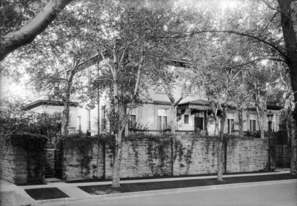 View of the Albert E. Humphreys residence at 1022 Humboldt Street in the Cheesman Park neighborhood of Denver, Colorado; shows a house with a walled yard, cornice, and a wrought iron and glass canopy.