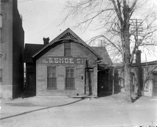 View of a house on 11th (Eleventh) Street in the Auraria neighborhood of Denver, Colorado; formerly the David H. Moffat residence and business. Sign reads: "Al's Shoe Shop." Bargeboard is in the gable.