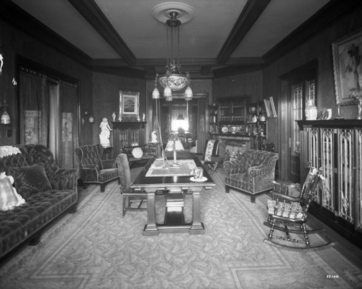 Interior view of the library at the David H. Moffat house at 808 Grant Street in the Capitol Hill neighborhood of Denver, Colorado. A sofa, chairs, table, bookcase, and fireplaces are in the room.