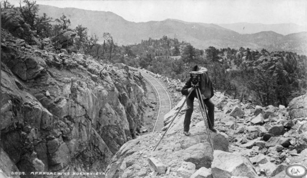 A Man looks through the back of a large format camera along the Colorado Midland Railway tracks near Buena Vista (Chaffee County), Colorado. The surrounding rock outcropping is probably part of Midland Hill.
