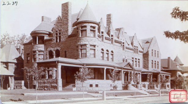 A view a building with four porch entrances.  The sandstone row house features towers, bays, porches, recessed porches, transom windows, arches, stone chimneys and a carriage portico.