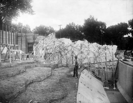 Workmen construct the bear habitat at the zoo in City Park, Denver, Colorado. A wooden frame and sawhorses are near the concrete cast.