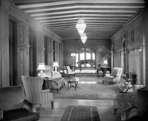 Interior view of Richthofen Castle at 7020 East 12th (Twelfth) Avenue in the Montclair neighborhood of Denver, Colorado. Chairs, a sofa, grand piano, and a palm tree are in the room.