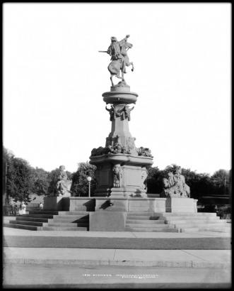 View of Pioneer Monument, intersection of Colfax, Broadway & Cheyenne Place, Denver, Colorado; behind statue is glimpse of Colorado State Capitol lawns and grounds.