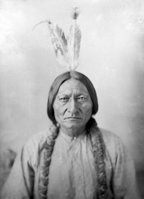 Studio portrait of head and shoulders of Sitting Bull, Dakota Chief, wearing two feathers in hair.