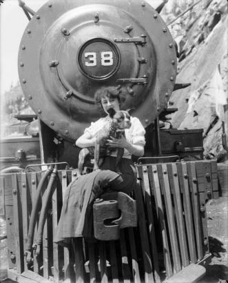 Singer and actress Anna Held is seated on the front of a train in Colorado Springs (El Paso County), Colorado. She holds a dog.