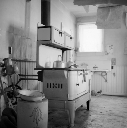 Interior view of the kitchen in Charles H. Harris (ranch homesteader) in Carbondale, Roaring Fork River Valley, Garfield County, Colorado; includes an enameled cook stove with kettles on top, a crock with  a decorative leaf pattern, meatgrinder (?), and wood panel wainscot.