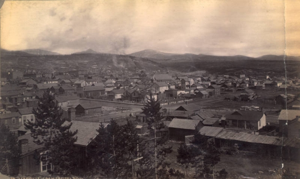 View of Leadville (Lake County), Colorado from Capitol Hill, an upscale residential neighborhood. Shows smoke from a smelter chimney, residences, and a sign on a backyard fence: "Smoke Little Joker Tobacco."